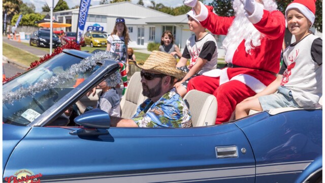 Image © Claude Thérond – used with permission Santa riding in a blue convertible with kids during a sunny Christmas parade.