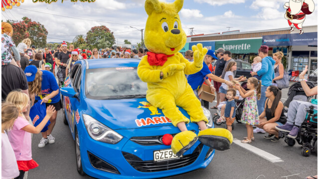 Image © Claude Thérond – used with permission Yellow mascot waving from blue car at Pohutukawa Coast Santa Parade